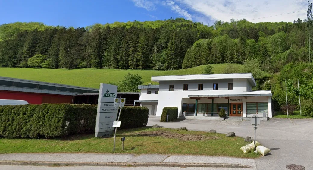Weißes Bürogebäude mit der Aufschrift Möbelstudio, daneben die Werkhalle und der Pylon der Tischlerei Winter
