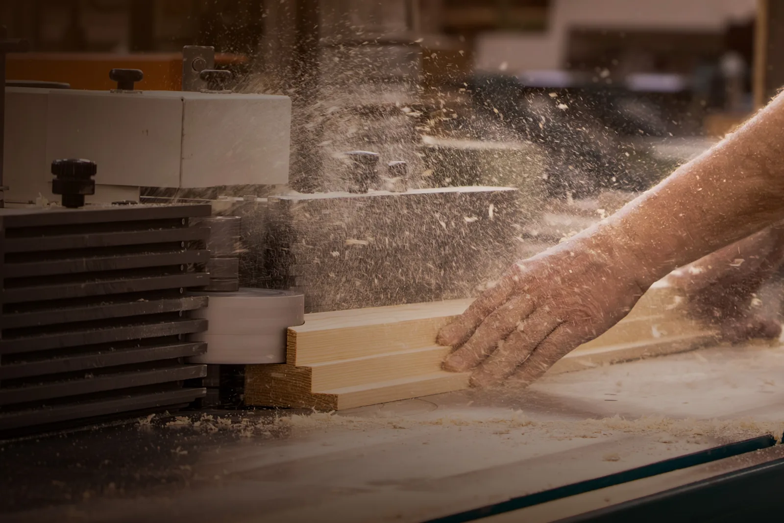 Hände schieben eine Holzleiste durch die Maschine, feine Späne fliegen